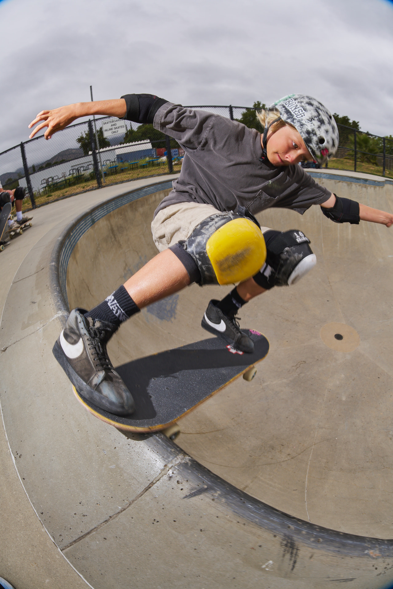 Skater in helmet, knee and elbow pads carving the lip of a bowl